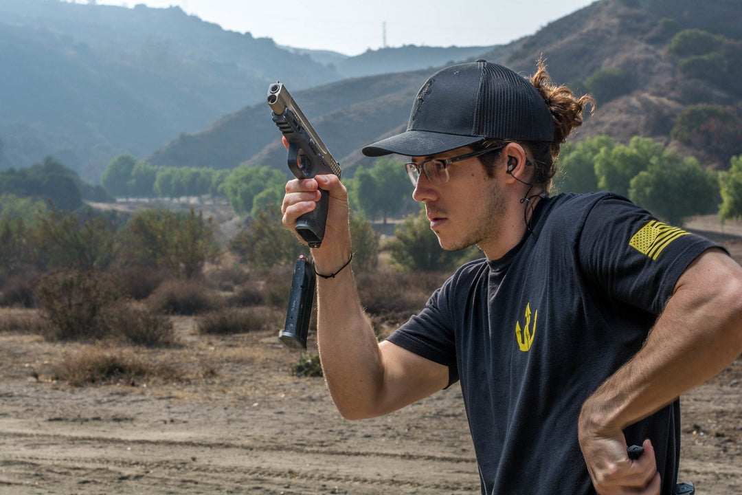 Man demonstrating a quick magazine reload on a handgun at an outdoor shooting demonstration.