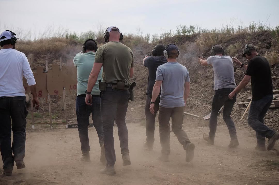 Men in line shooting handguns at an outdoor shooting range.