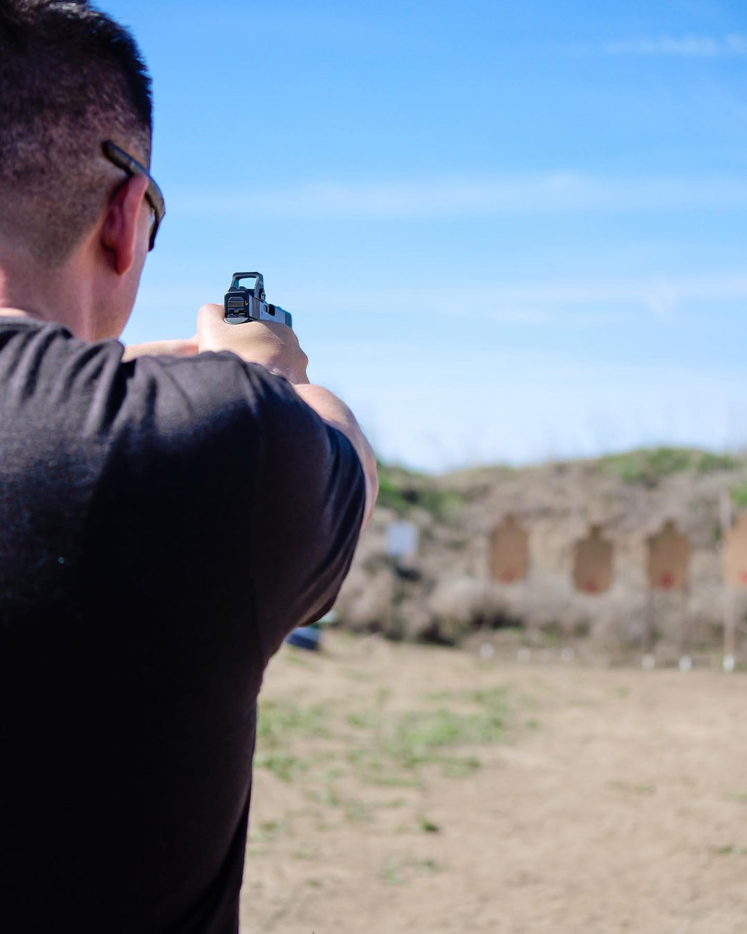 Man with a handgun aiming at targets at an outdoor shooting range.