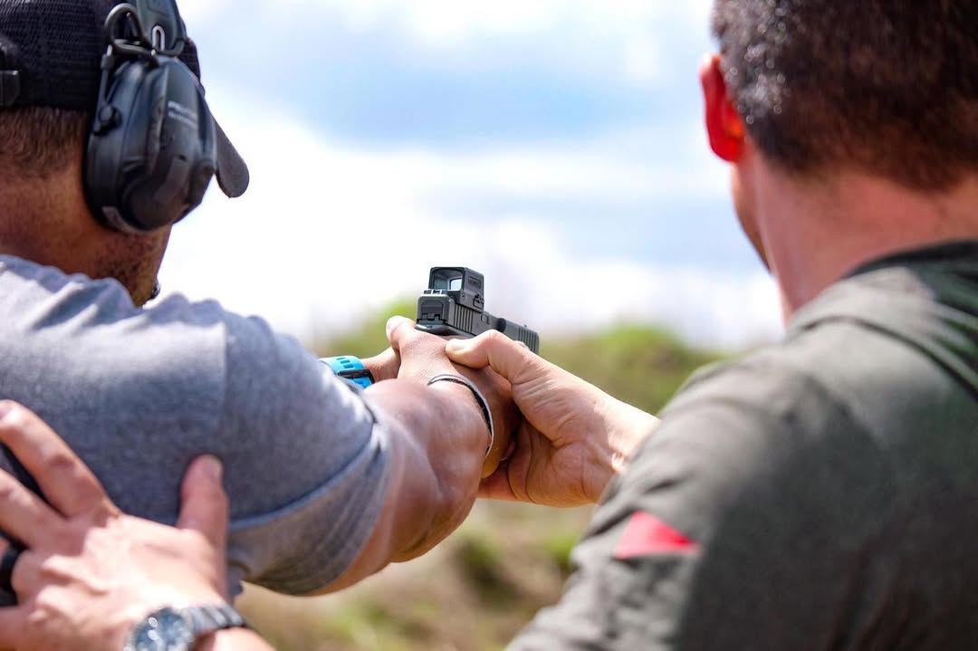 Man assisting with red dot sight focus during a handgun training demonstration.