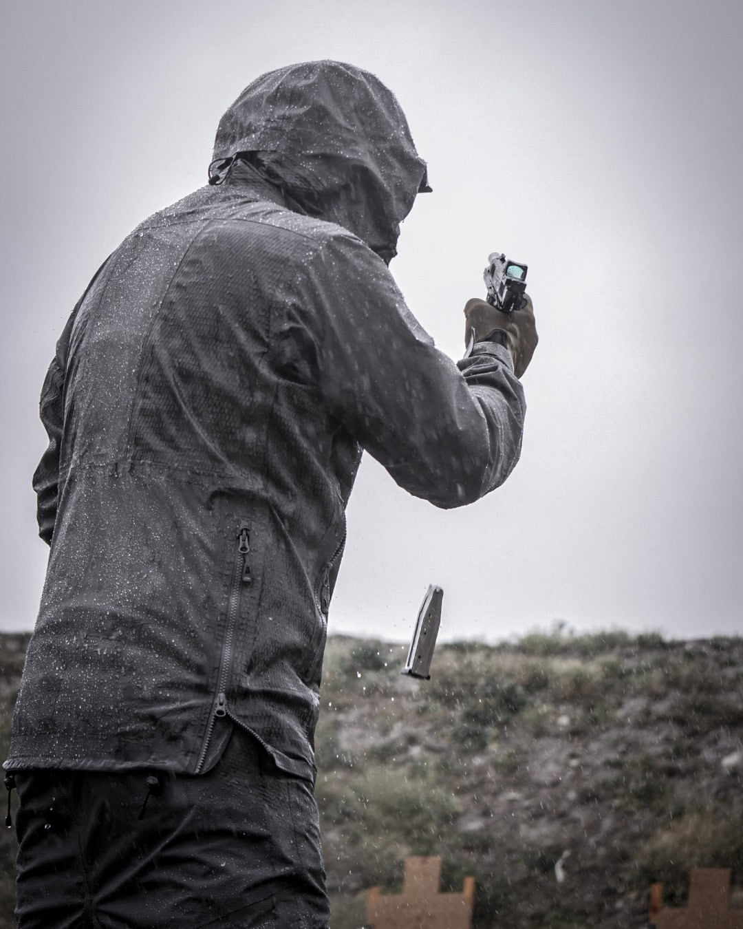 Man reloading a magazine into his gun in the rain during a self defence training demonstration.