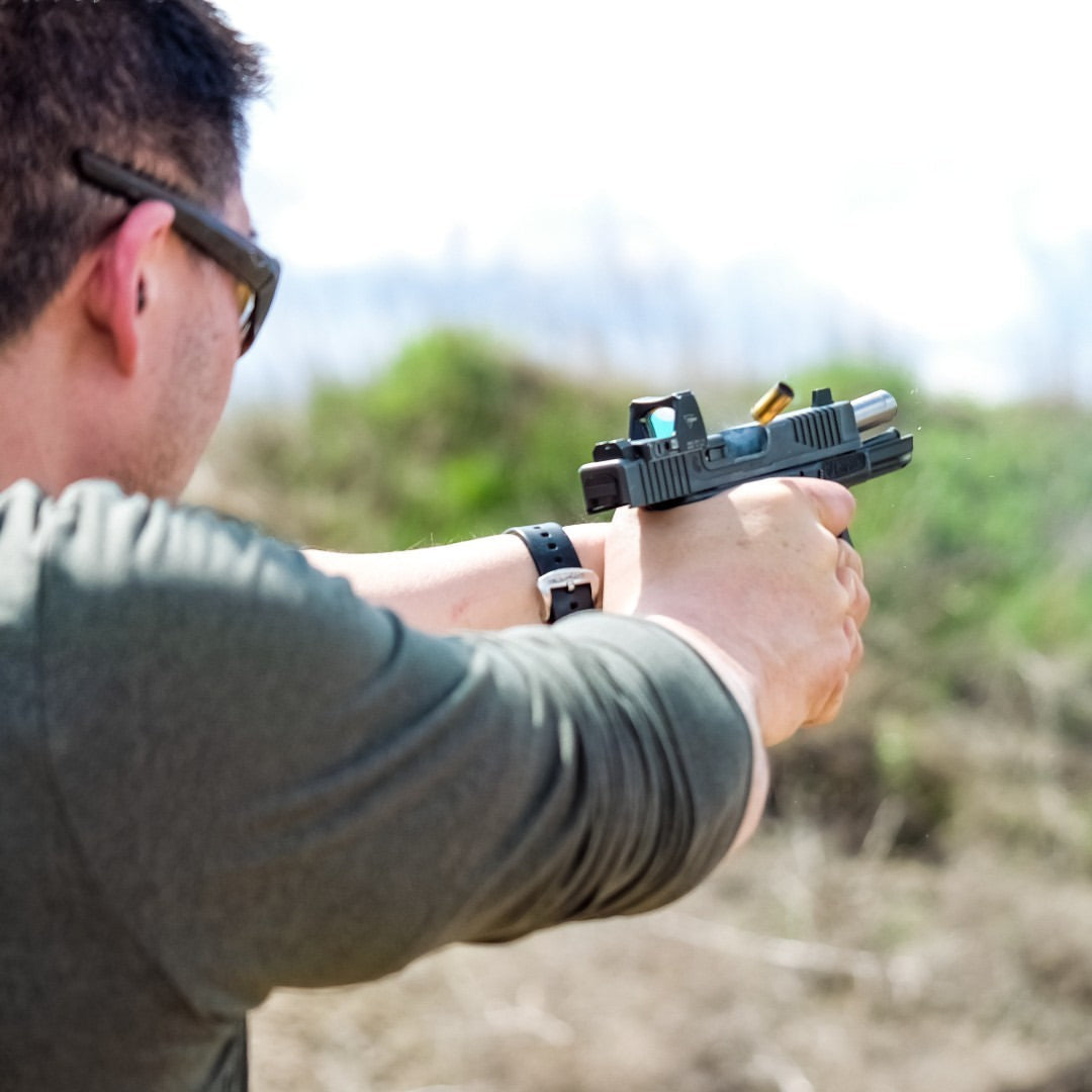 Man firing a handgun at an outdoor shooting range.