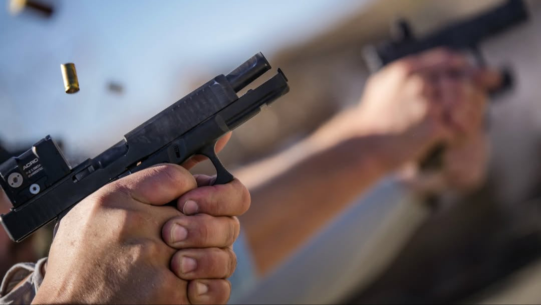 Hand holding a handgun with bullets flying around, blurred background