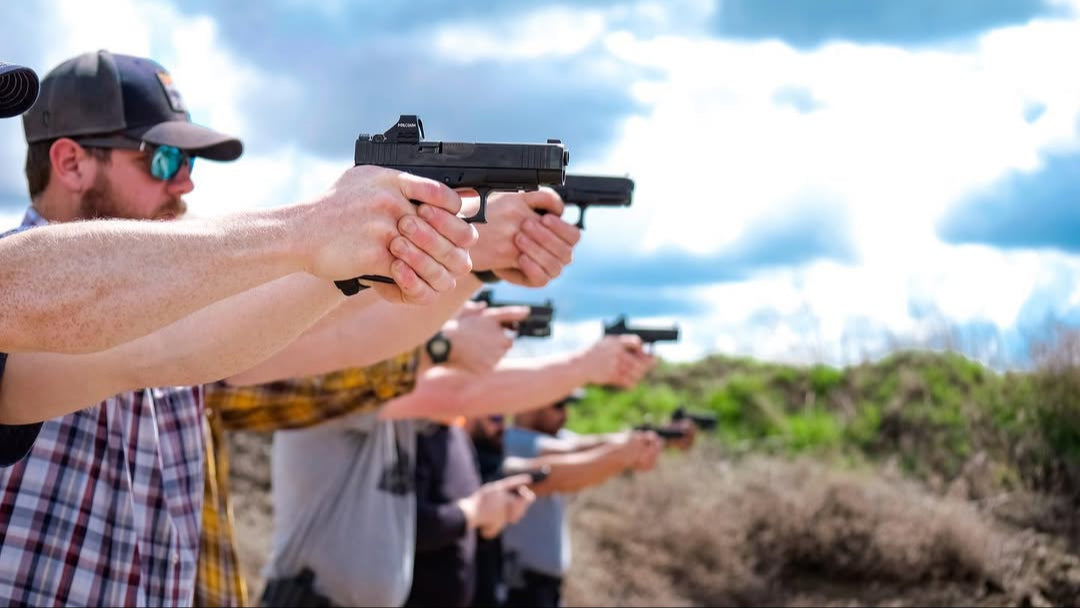 Group of people holding firearms outdoors with a clear sky.